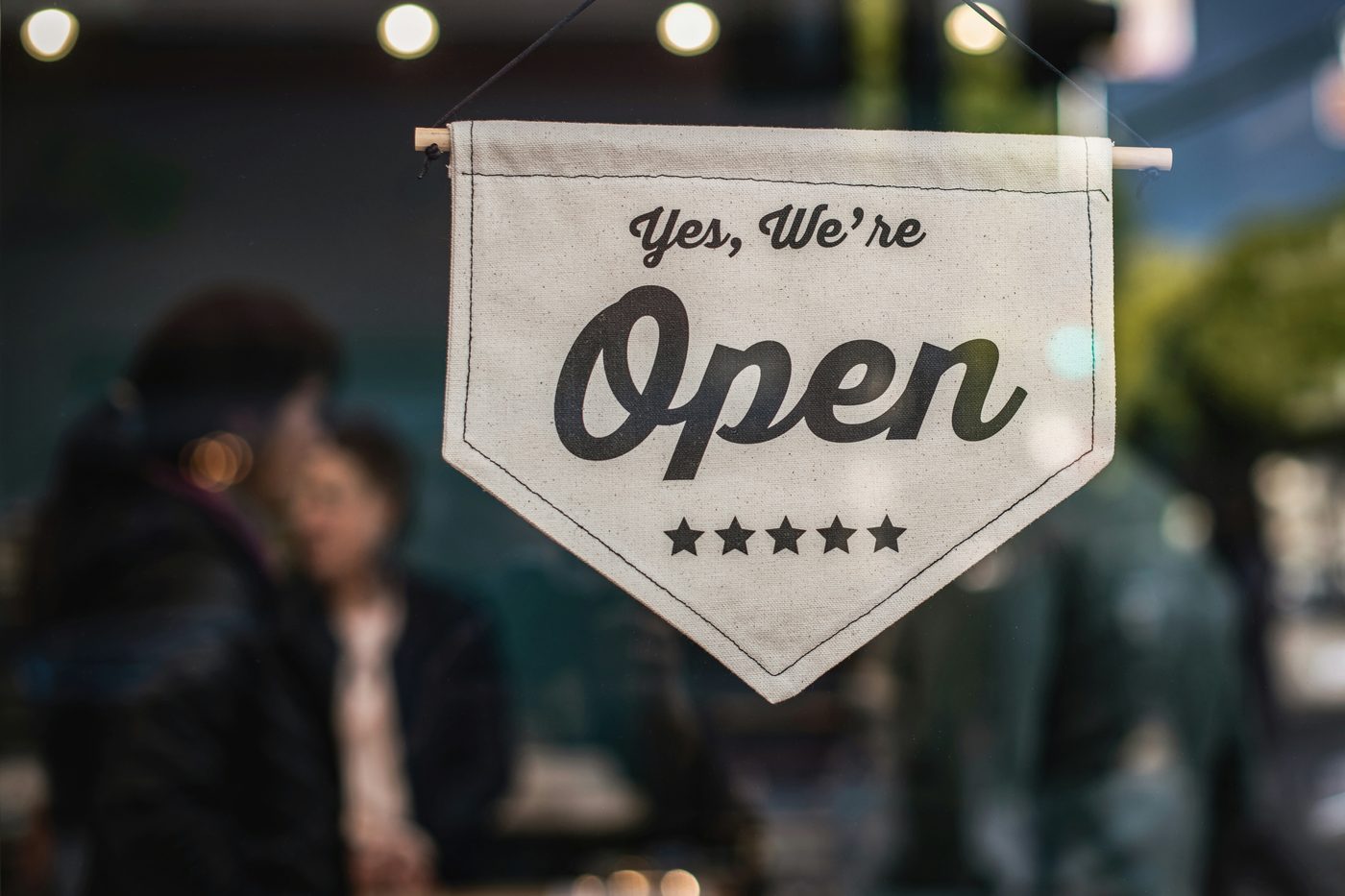 A canvas banner hanging in a shop window reading Yes, We're Open.