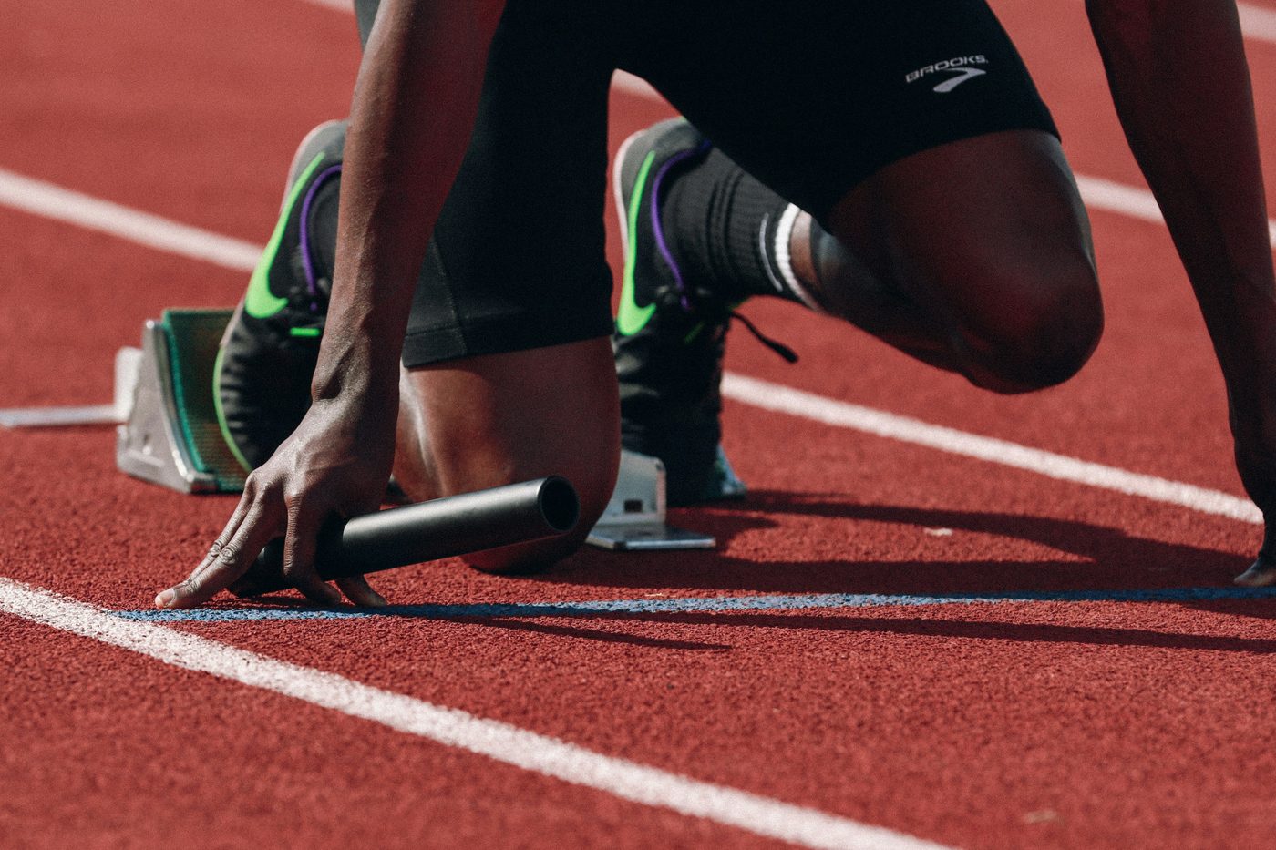 A sprinter set in the starting blocks holding a relay baton.
